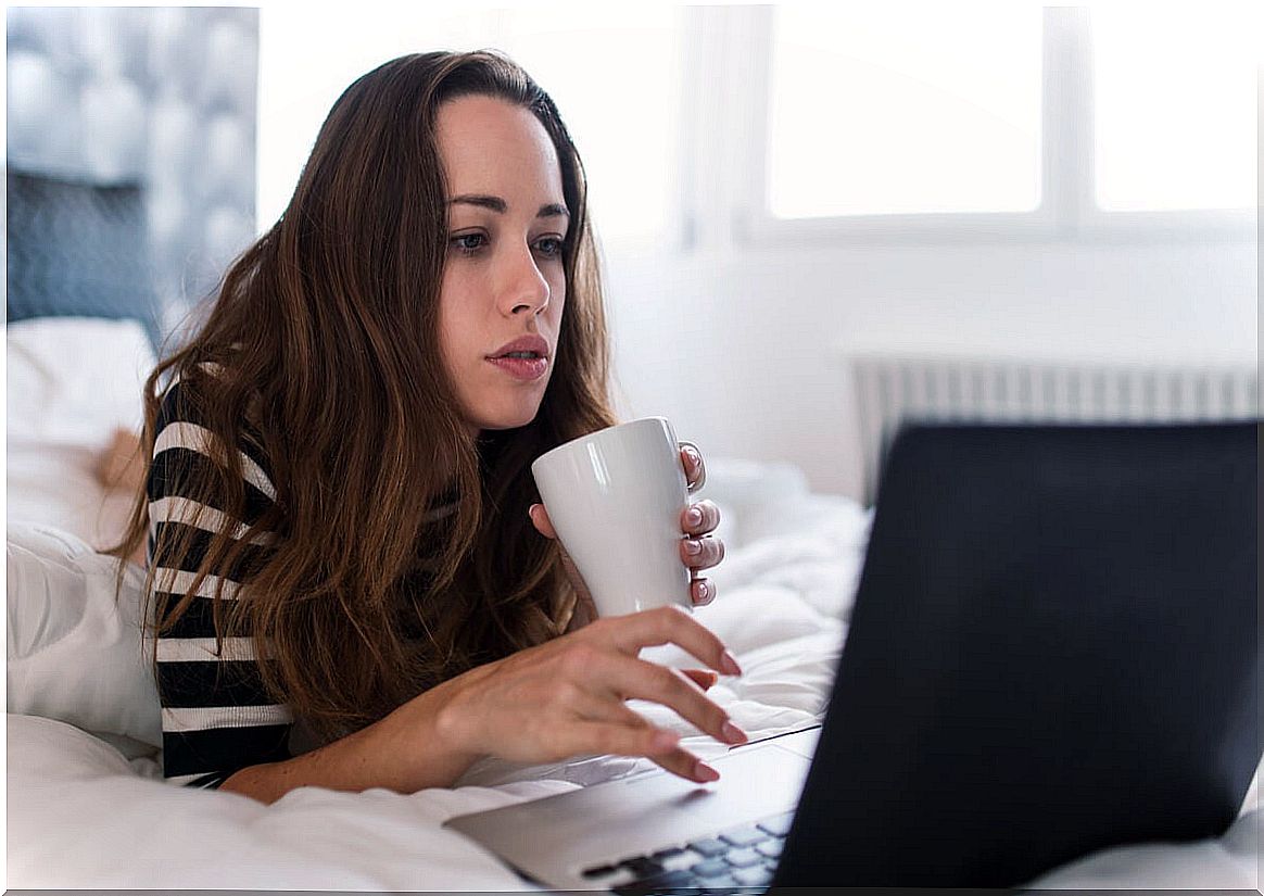 Woman works from home on her bed with a computer.