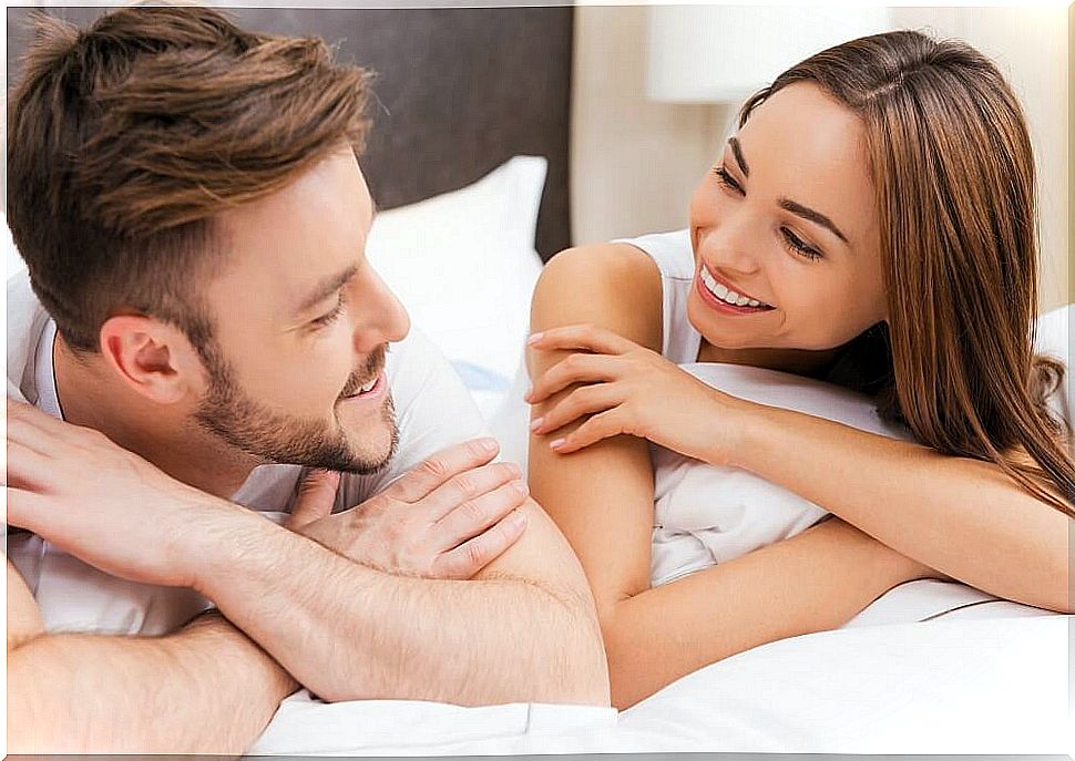 Couple looking at each other and smiling on top of the bed